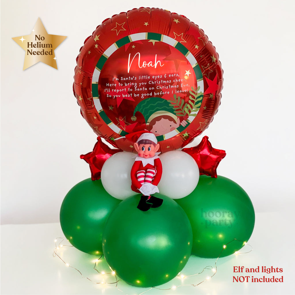 Elf arrival balloon stack kit with green, white and red balloons displayed with elf and Christmas fairy lights.